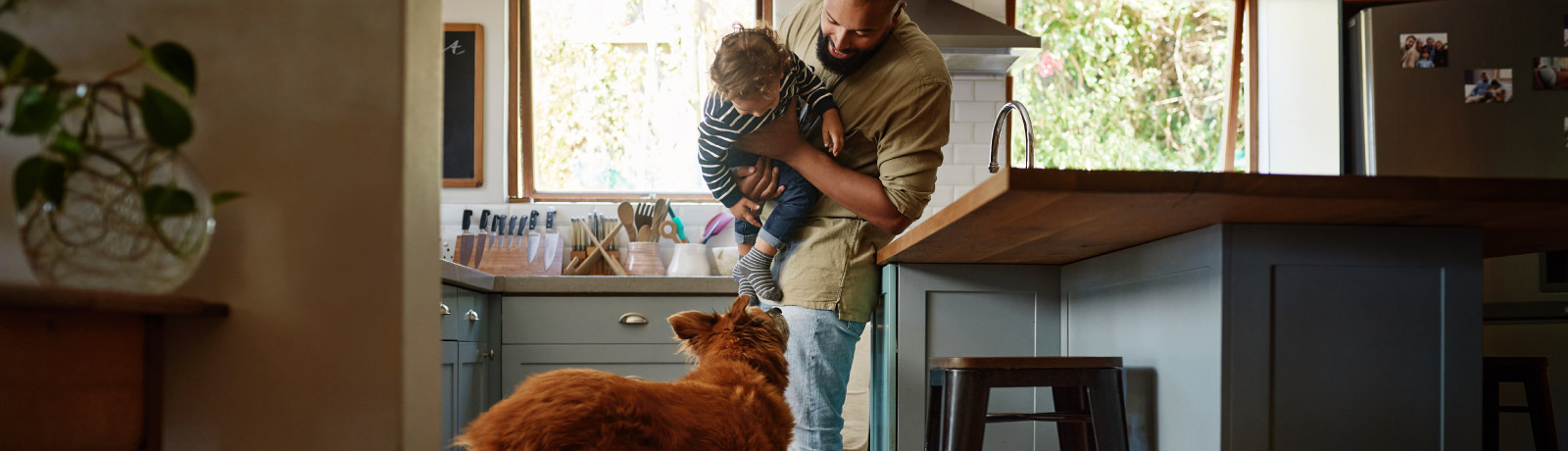 father holding his son in the kitchen with a dog
