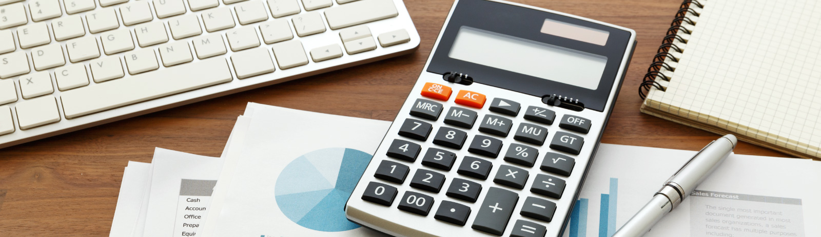 calculator sitting next to a keyboard, pen and notebook