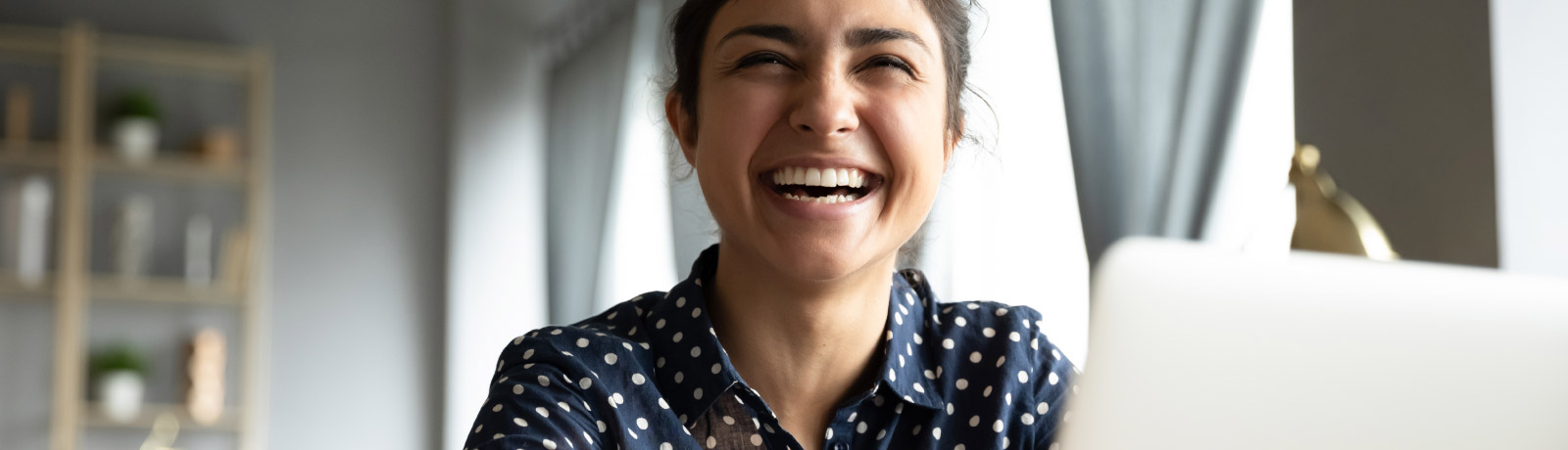 a woman laughing sitting in front of her laptop